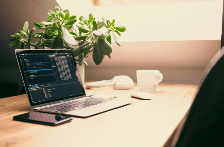 Робочий стіл з ноутбуком, телефоном, чашкою кави та квіткою в горщику — символ початку дій і перших кроків після декрету.